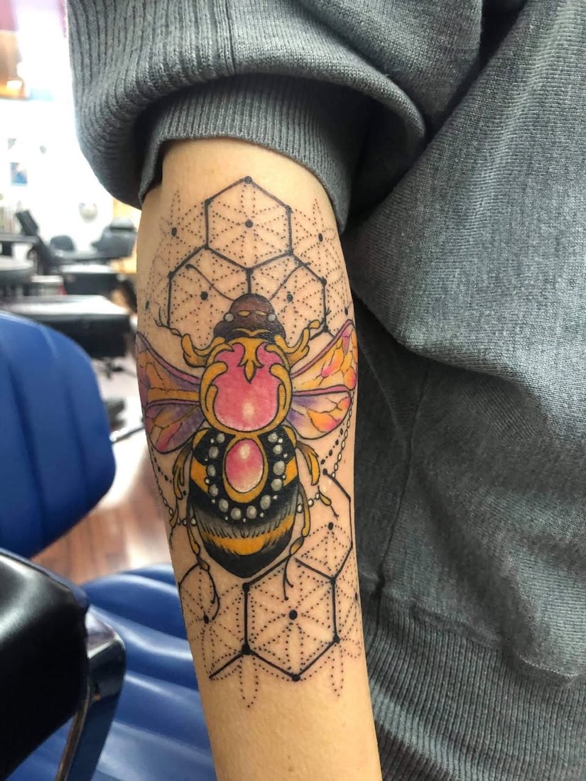 Color arm tattoo of a bee over a geometric honeycomb pattern