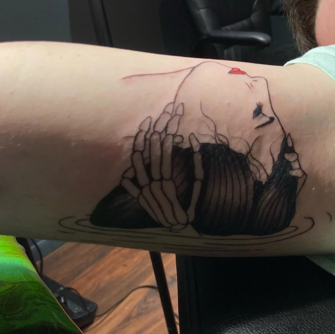 Linework arm tattoo of skeleton hands holding a woman's face with red lips