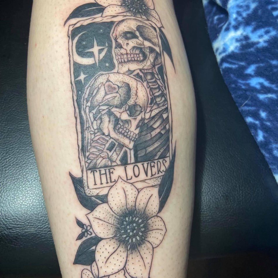 Calf tattoo of a 'The Lovers' tarot card with two skeletons above a flower
