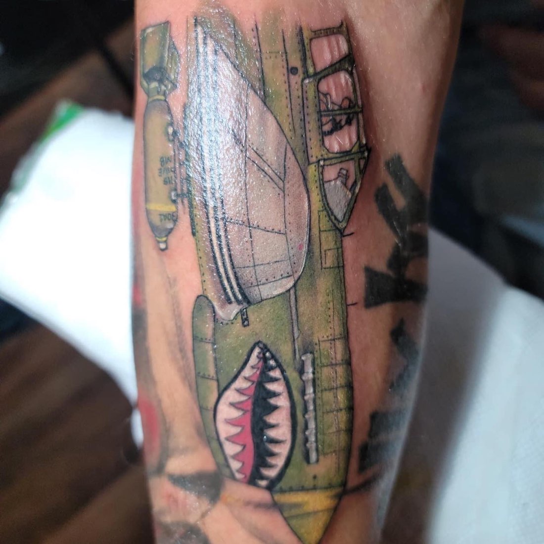 Color forearm tattoo of a vintage bomber plane with shark-tooth nose art