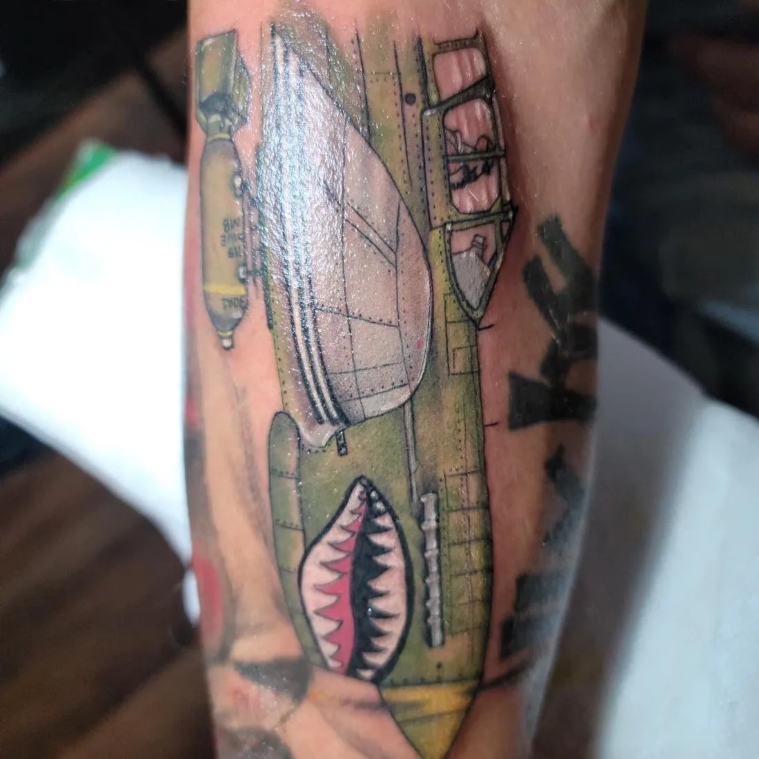 Color forearm tattoo of a vintage bomber plane with shark-tooth nose art