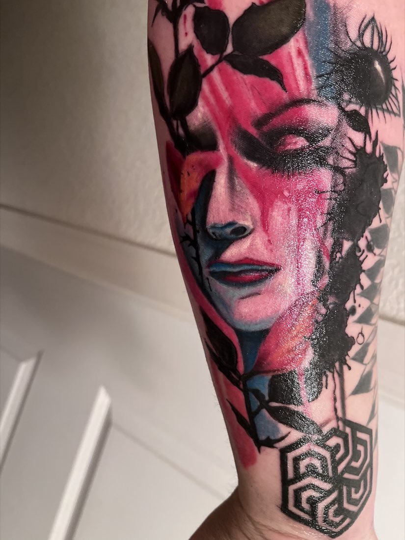 Forearm tattoo of a woman's face in pink and red with black leaves