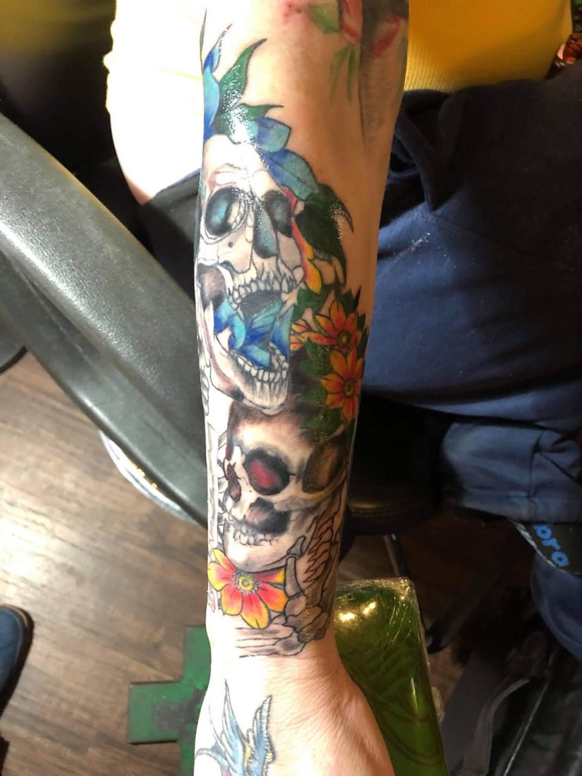 Color forearm tattoo of stacked skulls with orange flowers