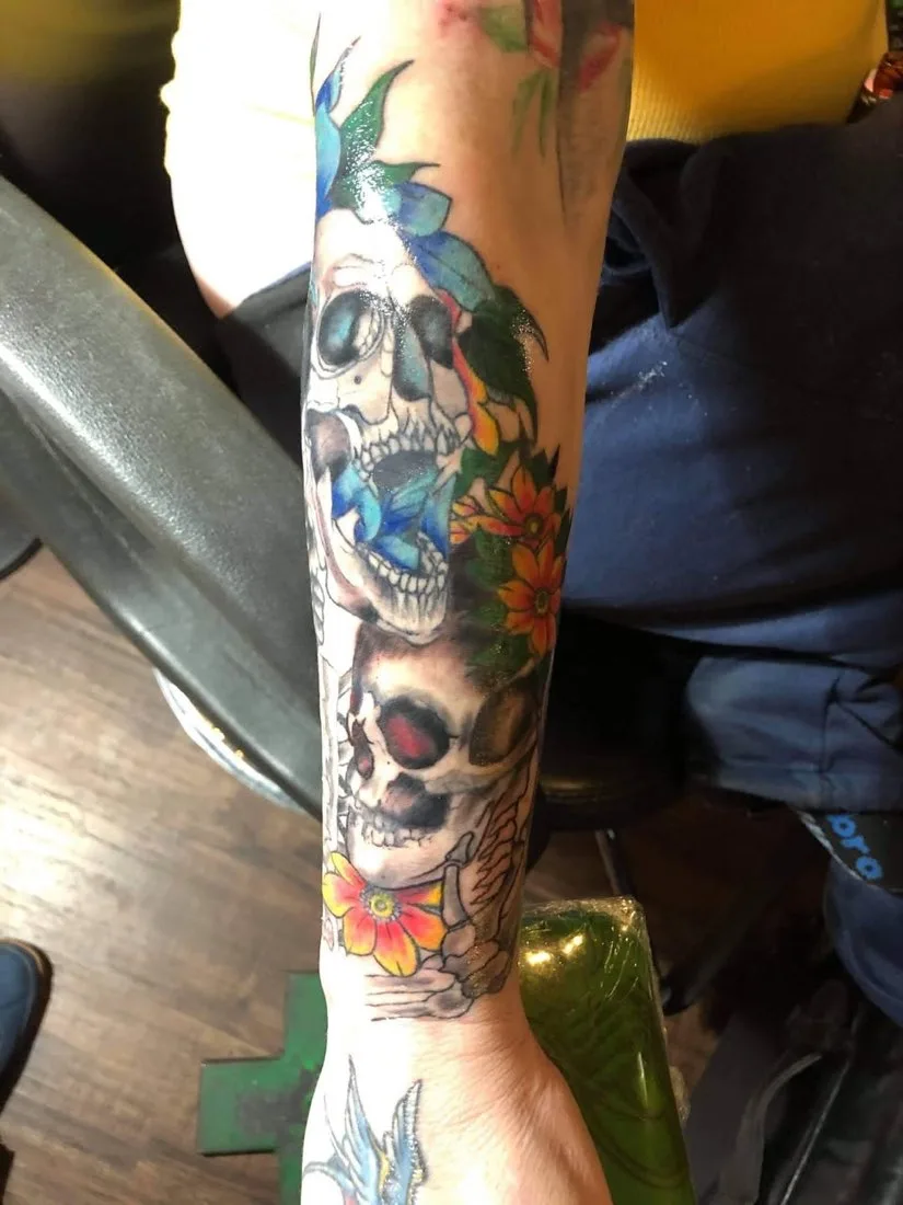 Color forearm tattoo of stacked skulls with orange flowers