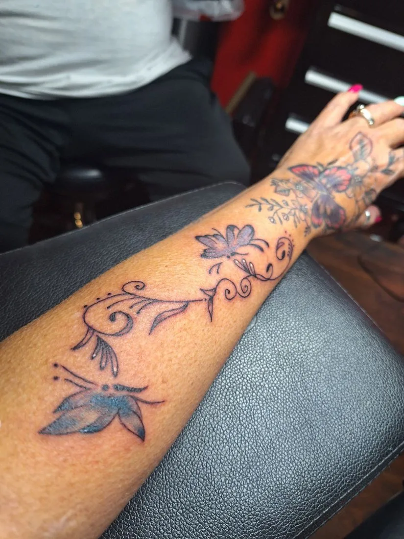 Forearm tattoo of a flowering vine with a butterfly
