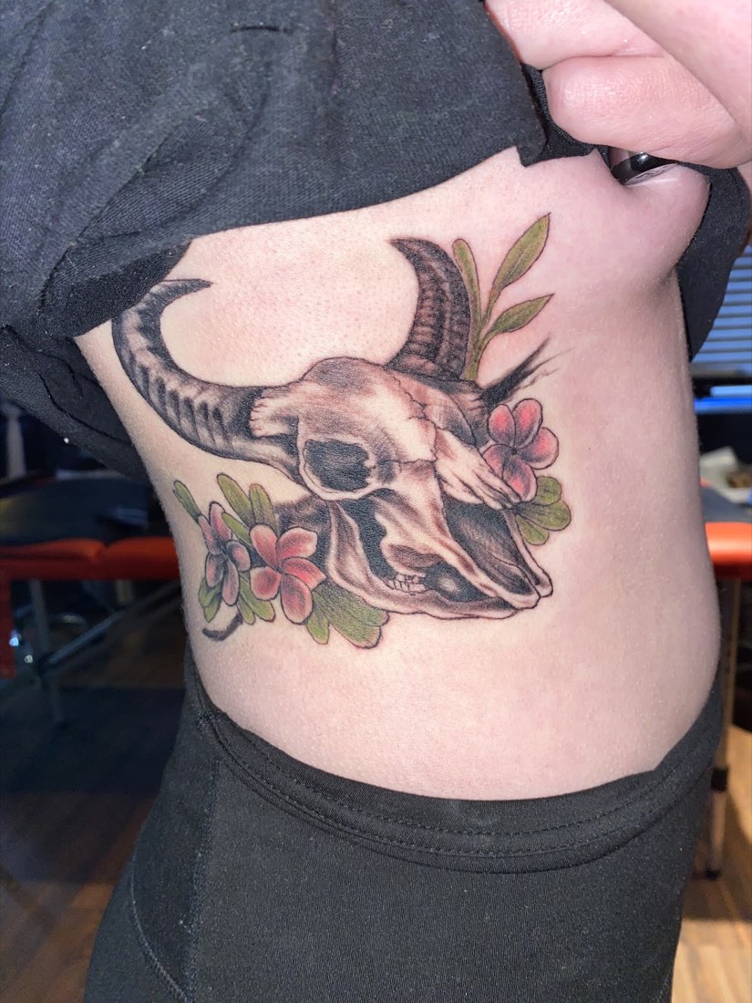 Rib tattoo of a horned animal skull with pink flowers